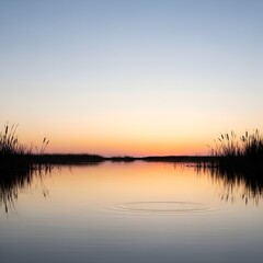 Obraz premium Serene Sunset Over Calm Lake with Silhouetted Reeds Reflecting in Water.
