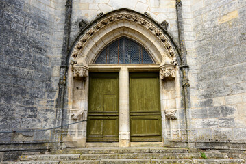Fototapeta premium A weathered green double door set within a pointed stone archway forms the entrance to an old church in Pouilly sur Loire. Intricate Gothic details and aged masonry create a sense of heritage and