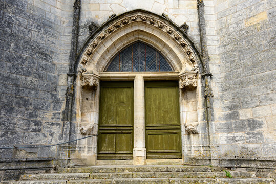 A weathered green double door set within a pointed stone archway forms the entrance to an old church in Pouilly sur Loire. Intricate Gothic details and aged masonry create a sense of heritage and
