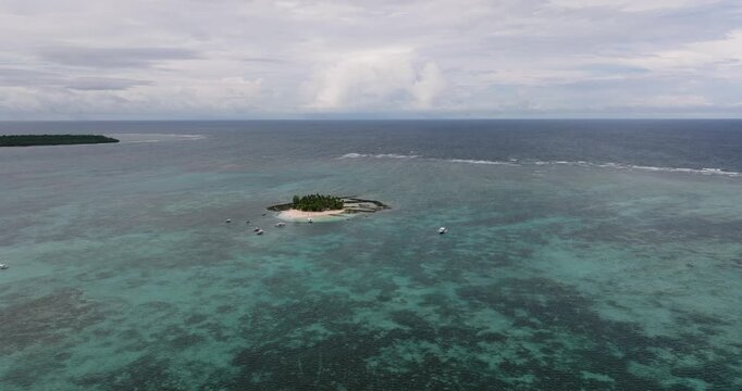 Island with palm trees surrounded by turquoise sea, boats anchored nearby. Guyam Island. Siargao, Philippines.