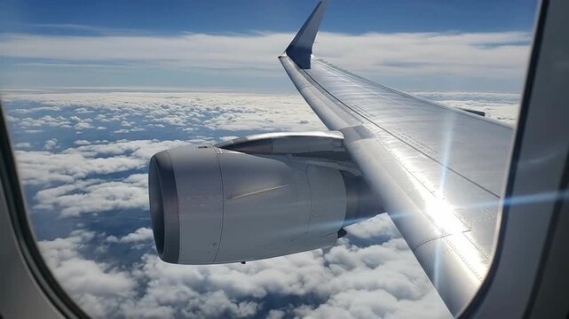 Airplane wing and engine are seen through the window during a flight above the clouds.