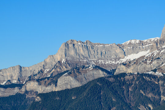 Imposing limestone cliffs of Aup de Veran rise above dense pine forests, their rugged faces catching the crisp winter sunlight under a vivid blue sky.
