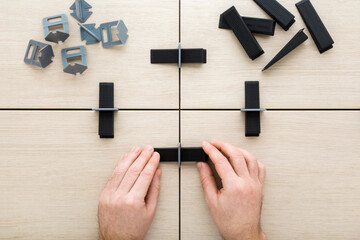 Man hands connecting plastic clips and wedges for floor or wall tiles surface leveling. Beige ceramic tiles gluing. Closeup. Renovation process. Repair work of home. Point of view shot. Top down view.