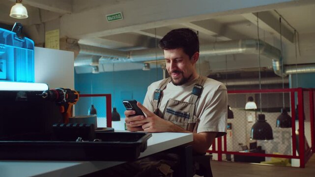 Worker checks phone and organizes tools in workshop during daytime in a modern space