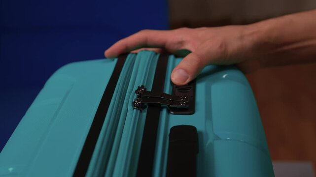 Secure suitcase with combo lock, Hands set combination on teal suitcase with textured surface, Closeup of hands adjusting numeric lock on stylish teal travel suitcase