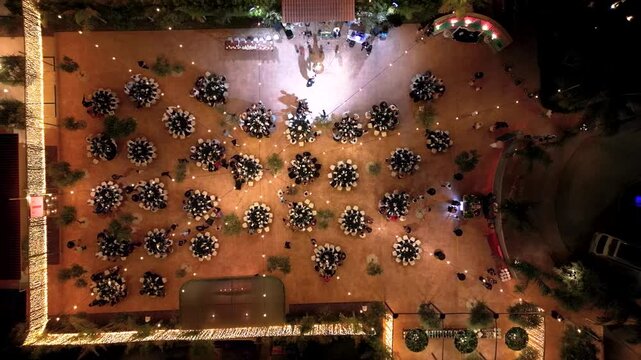 Guests gather at an outdoor dining event with numerous tables set up under lights. The atmosphere is lively as people enjoy their meals and socialize in the evening.