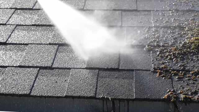 A high-pressure cleaner blasts away debris on a weathered roof. The stream of water removes dirt and moss, revealing a clean surface. The cleaning process is shown
