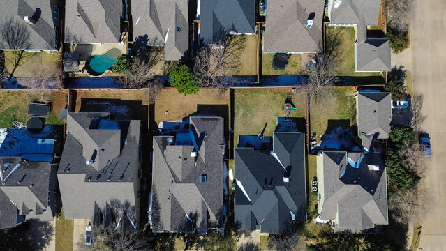 Neighborhood south of FM 407 forms tight grid of fenced backyards with varied seasonal features. Mixed shingles, snow patches, dormant grass, soft daylight highlight winter textures, Lantana, TX