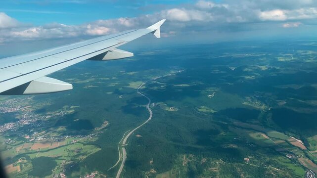 Passenger Plane Wing in Blue Sky Above Clouds, Scenic Landscape Below
