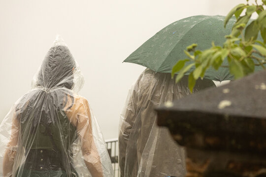 Pessoas vestidas com capa de chuva e guarda chuva em um dia chuvoso. 