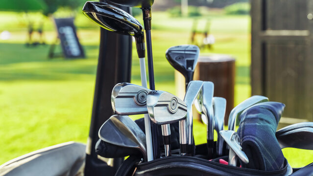 Golf clubs are ready in a bag beside a green field where people play golf on a sunny day