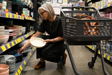 Woman shopping for bowls in a retail store with shopping cart and focused look on her face
