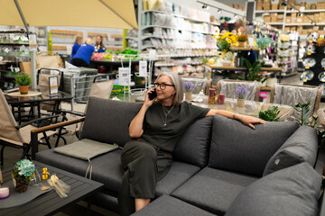 Senior woman enjoys shopping while talking on the phone in a bright garden center room filled with plants and decorations