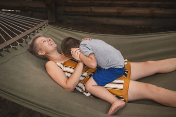 Naklejka premium mother son 5 years old fooling around playing relaxing in hammock outdoors in pine forest at camp. Tourism, active recreation, time spent with children. Real emotions, pleasant aspects of motherhood