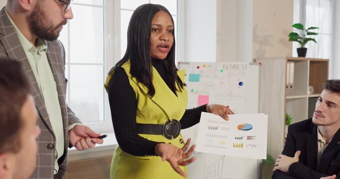 Woman leads presentation at team business meeting. In a bright office she shows charts, framing strategy and planning that involve coworkers. Teamwork drives measurable business success.