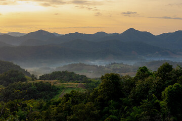 Countryside landscape, Big mountains, forest and farmland under warm sunlight, Wonderful sunrise in the morning with golden yellow skyline, Mueang Mai, Chae Hom District, Lampang province, Thailand.