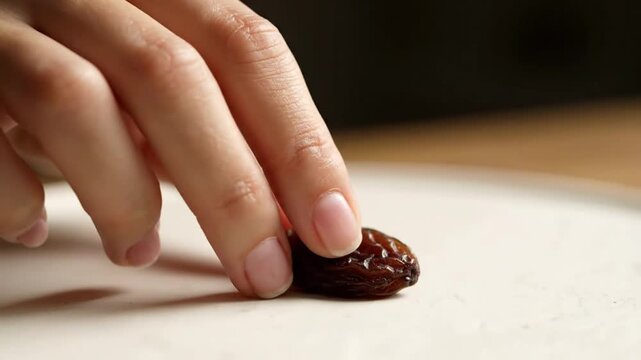 Hand holding date fruit on white surface.