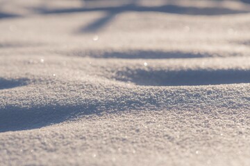 A close-up view of sparkling snow crystals, softly illuminated by sunlight, creating a bright, textured winter background with a serene and minimalist feel