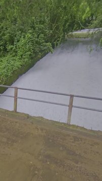 Vertical video of powerful milky white water rushing through a dam canal sluice gate in Agartala Tripura. High angle view of turbulent irrigation water flow creating foam and splashes in 4K.