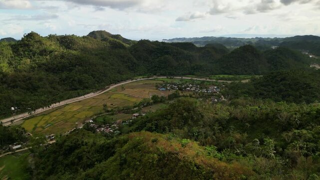Stunning aerial drone shot of quaint barangay village and farmland amid lush rolling hills at Catanduanes, Philippines.
