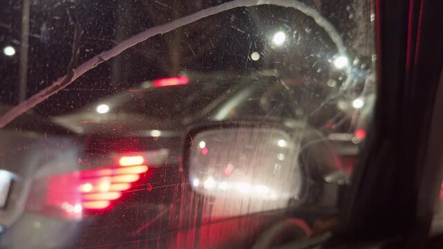 Wet window reveals congested street scene. Misty evening with red streaks and glowing halos