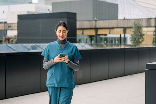 Female nurse checking smartphone walking in urban area