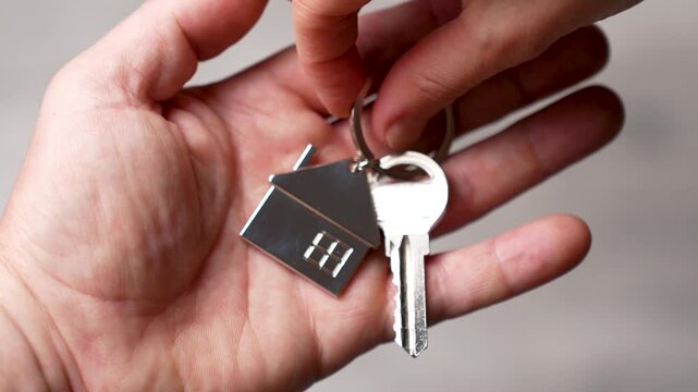 Handing Over House Keys to New Homeowner. Close-up of one person's hand placing a house key with a house shaped keychain into another person. Concept for real estate closing and property handover.