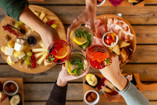 Friends toasting, cocktail glasses, wooden table, snacks, happy hour, lifestyle, socializing, beverage advertising