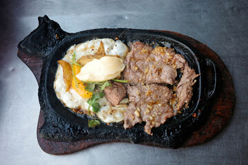overhead view of authentic vietnamese sizzling steak called bo ne served on a unique cow shaped cast iron hot plate with fried egg pate and butter representing local street food culture