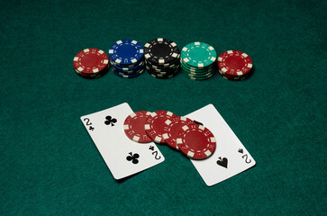 Two playing cards show the number two in a poker game. Various colored chips are stacked behind the cards on a green felt table during a casino night