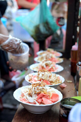 Fototapeta premium White bowls of Indonesian chicken porridge featuring shredded chicken, pink crackers, and fried shallots arranged on a wooden surface, with a vendor's hand visible in the shallow depth of field.