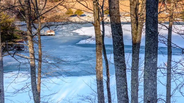 Timelapse shows a view through the forest trees of a frozen lake in Tennessee cracking and melting as temperatures rise above freezing.