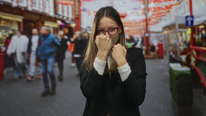 Fototapeta premium Woman in black blazer holds fists up in a boxing guard on a crowded street; confidence self defense training.