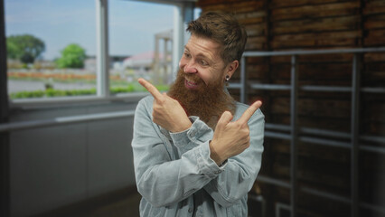 Naklejka premium Man with long ginger beard pointing both index fingers to the side in bright studio; enthusiasm celebration.