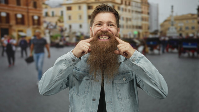 Man with a long beard pointing finger to teeth on a busy street amid urban buildings and passing crowds; playfulness.