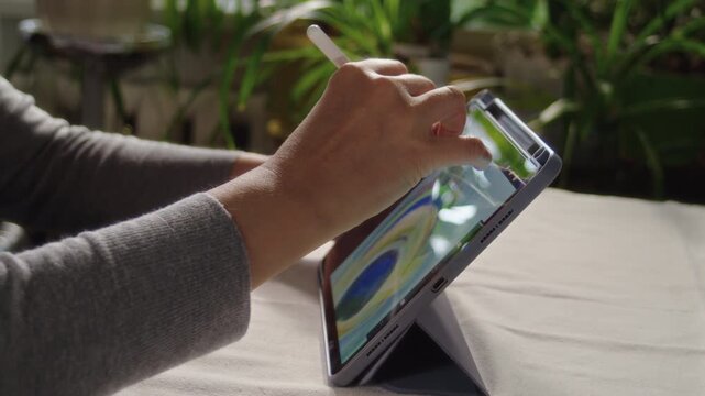 Close-up, artist drawing peacock feather on tablet screen while sitting at table in room