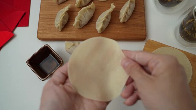 Hands preparing traditional Chinese dumplings with wrappers and filling on a clean table.Asian home cooking process, food preparation concept for Chinese New Year, family cooking,and homemade cuisine.