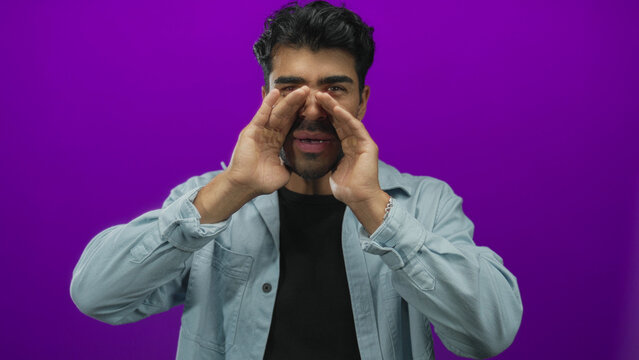 Man shouting with hands cupping mouth on a purple studio set, wearing a light denim shirt and expressive facial gesture; urgency.
