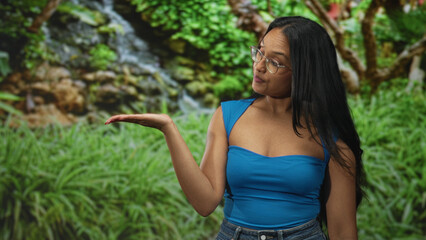 Fototapeta premium Woman touches chin with hand, bare shoulder visible, crossed arms and palm up pose in studio; thoughtful curiosity.