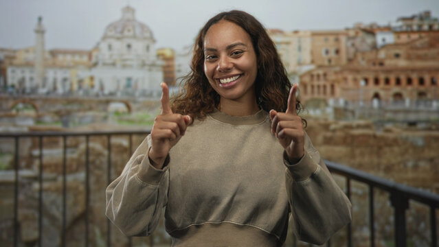 Woman smiling with finger pointing to camera in ancient roman building overlooking ruins and railing; joy travel discovery.