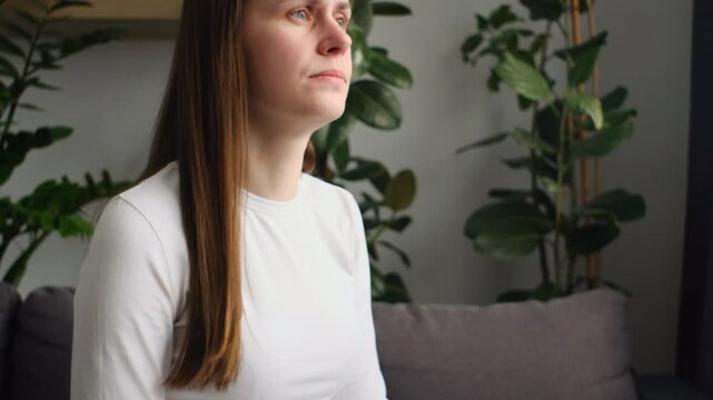 Upset worry young woman holding splitting ends, messy unbrushed dry hair and frizzy with disheveled hair sitting on sofa at home. Damaged hair. Health care of beauty concept