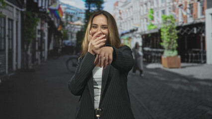Fototapeta premium Woman clapping hands and laughing, smiling broadly and pointing toward the camera on a bustling cobblestone street lined with cafes and a bicycle; joy.
