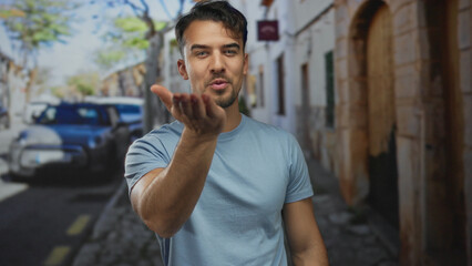 Fototapeta premium Young man in blue shirt smiling and blowing kiss on sunny city street.