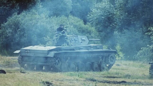 Detailed view of German Panzer III medium tank replica, foliage camouflage, commander visible, moving through smoke on dry field, depicting historical World War II military action.