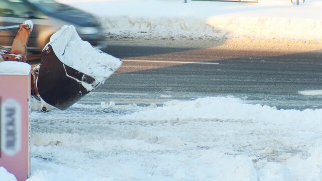 Orange front end loader fills dump truck with snow. Snow removal operation on winter day. Heavy equipment cleans road. Bright sunlight reflects off white snow. Municipal service work.