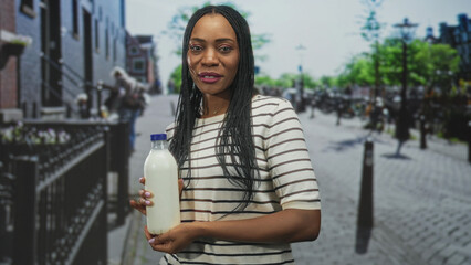 Fototapeta premium Woman holding milk bottle, hands cradling a glass bottle on a city street with railing and bicycles visible; nourishment calm.