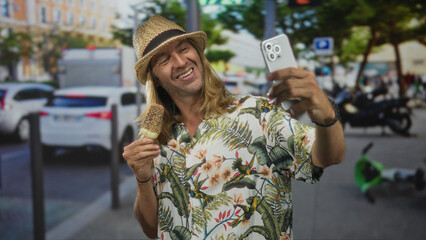 Fototapeta premium Man holds icecream cone and smartphone for selfie on downtown street market scene in vibrant city; vacation joy.