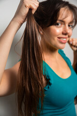 Obraz premium Young woman holds long hair and smiles while standing against a plain background