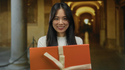 Naklejka premium Woman smiling with a gift outdoors at an old university campus with columns and arches in the background.