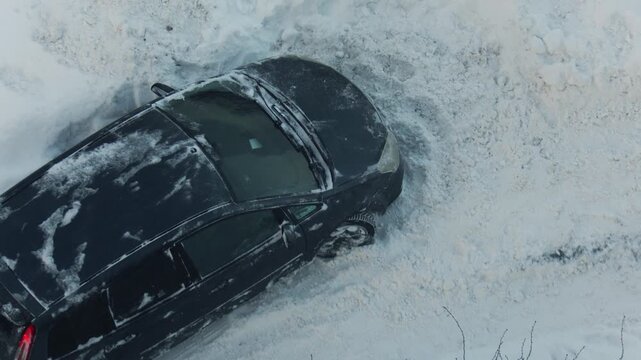 High angle view of dark color sedan stuck in massive snowdrift on unplowed road. Vehicle immobilized by winter blizzard and heavy snow accumulation, creating difficult situation for recovery.